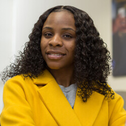 Headshot of Alexandra Kallan wearing a bright yellow coat, standing confidently against a neutral background