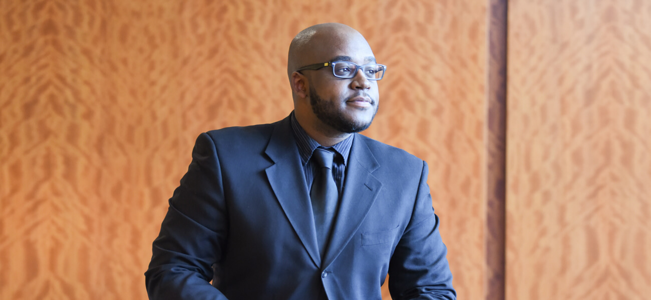 Photo of Alan “AJ” Watts wearing a suit and tie.