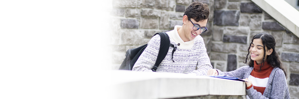 Male and female student reading a book on a ledge at the Woodland Park Campus
