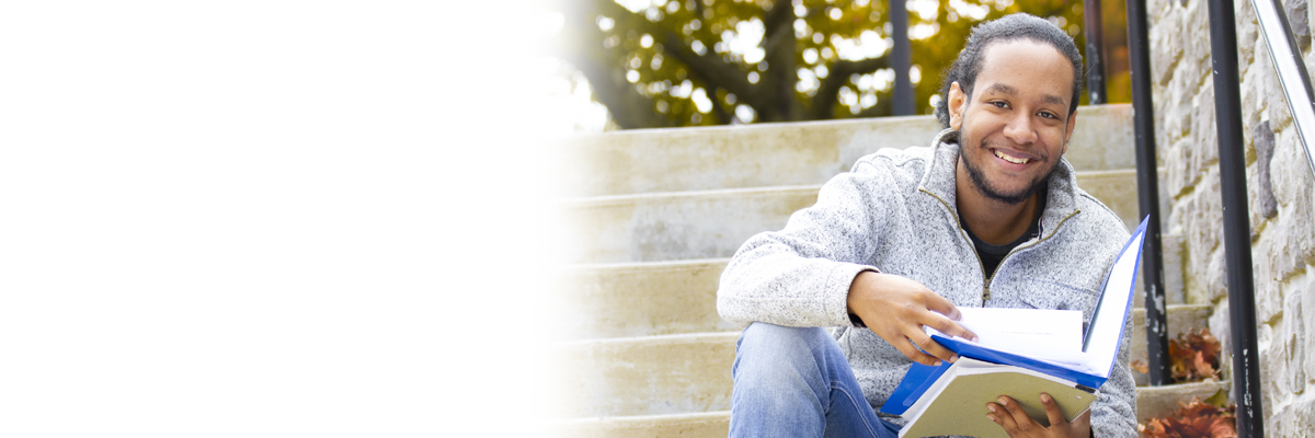 Photo of a male student holding a book while sitting down on campus steps mobile image