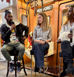 A panel discussion featuring three speakers in front of a NYC subway backdrop, with an audience engaged in the event.
