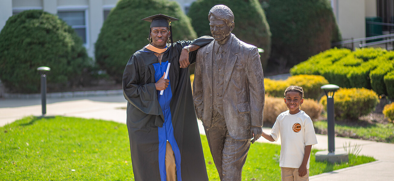 Berkeley College graduate Lamar Register and his son pose next to a campus statue.