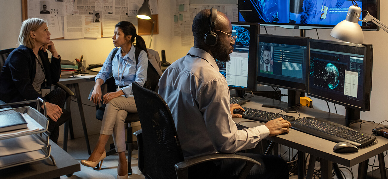 Three individuals seated at a desk, each using a computer, engaged in a collaborative work environment.