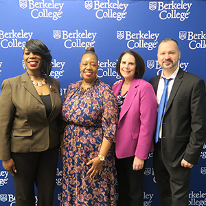 Four diverse people stand in a row and smile in front of a Berkeley College backdrop