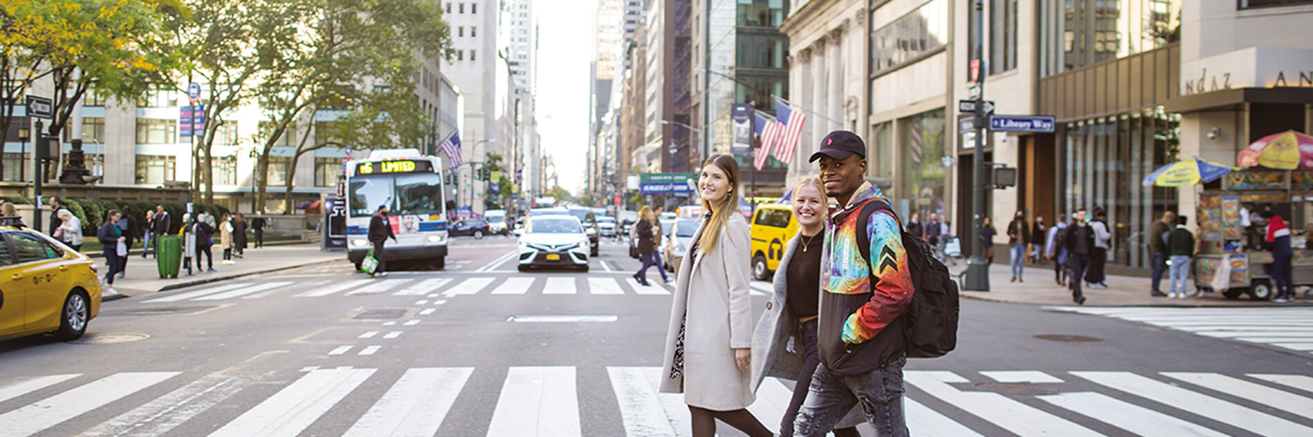 Image: Image: a busy traffic New York City street with three individuals crossing a crosswalk