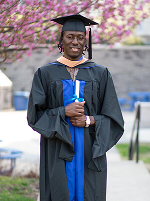 Berkeley College graduate Lamar Register smiles while holding his MBA diploma.