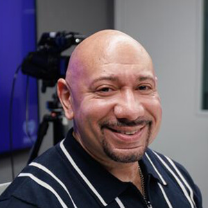 Man with a goatee smiles while speaking into a microphone during a podcast recording. Background features the Berkeley College logo and colorful graphics.