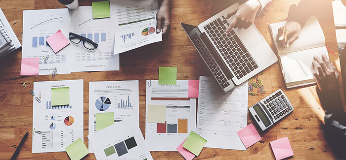 people working on a table with paper reports, a laptop and a calculator