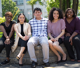 Image for mobile devices: Group of 5 students sitting on a wall outside of the Woodbridge campus