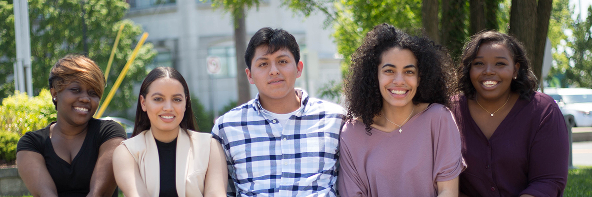 Image: Group of 5 students sitting on a wall outside of the Woodbridge campus