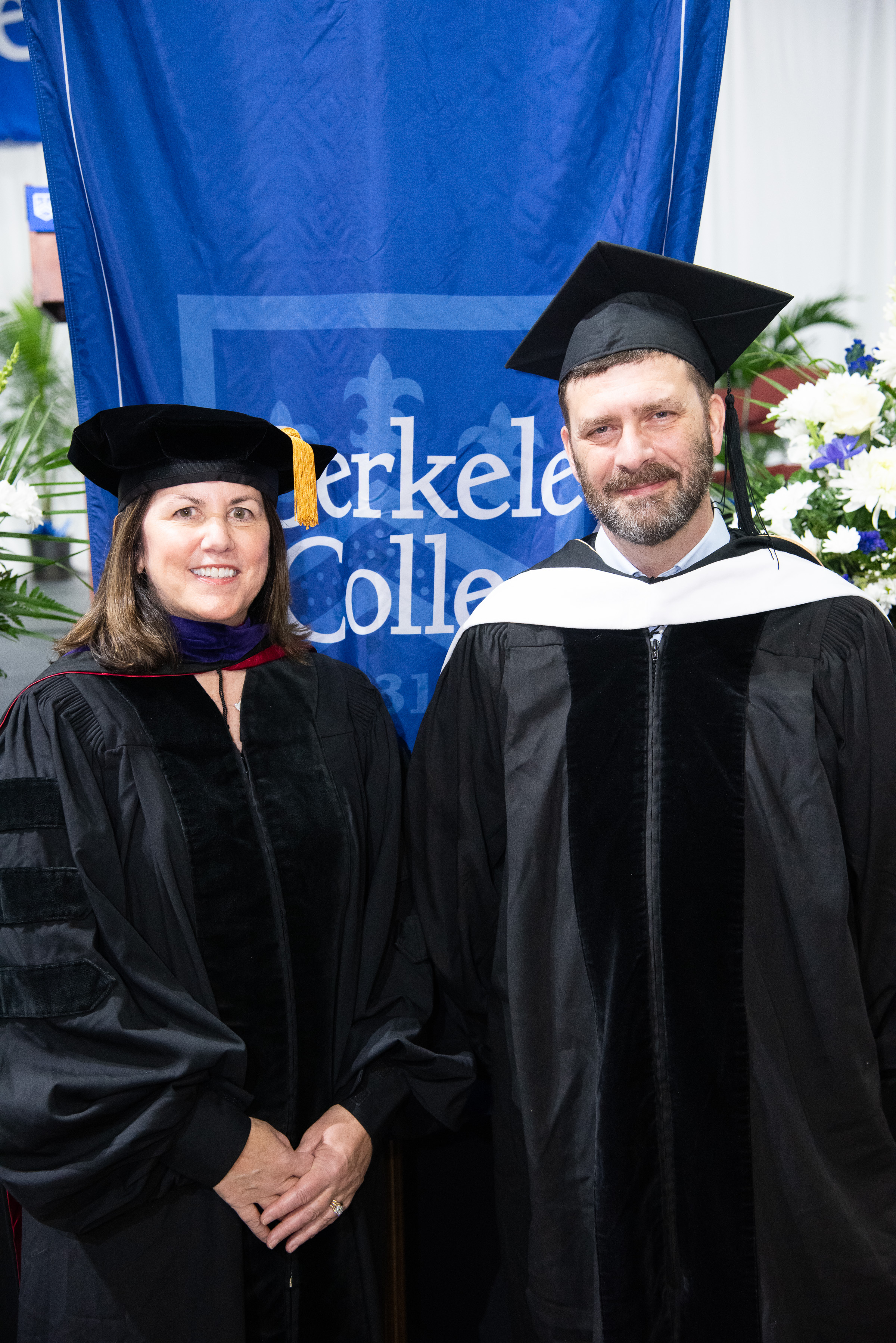 Berkeley College official stands with the Faculty Speaker in front of a Berkeley College banner