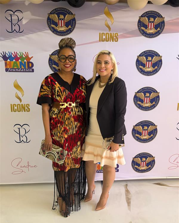 Two women stand in front of a backdrop for the Hand Foundation and President's Award