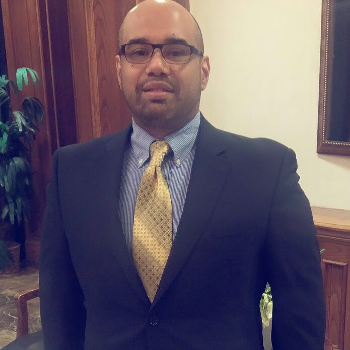 A man in a suit and tie smiles at the camera.
