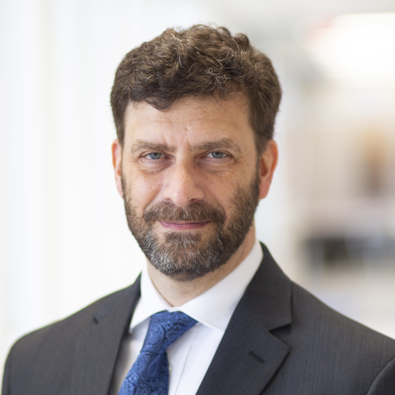 Richard Schultz stands in a hallway with a suit jacket and blue tie