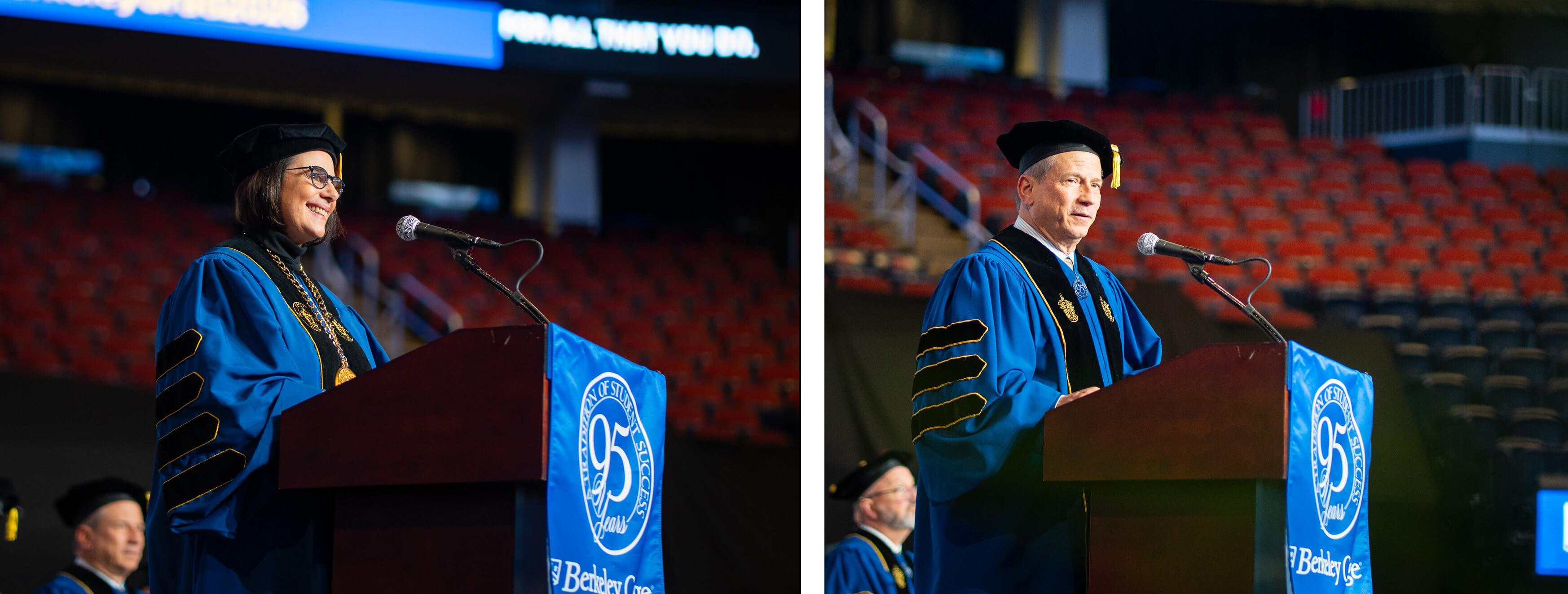 Two college officials in blue academic regalia speak at a podium during a graduation ceremony in an indoor arena.