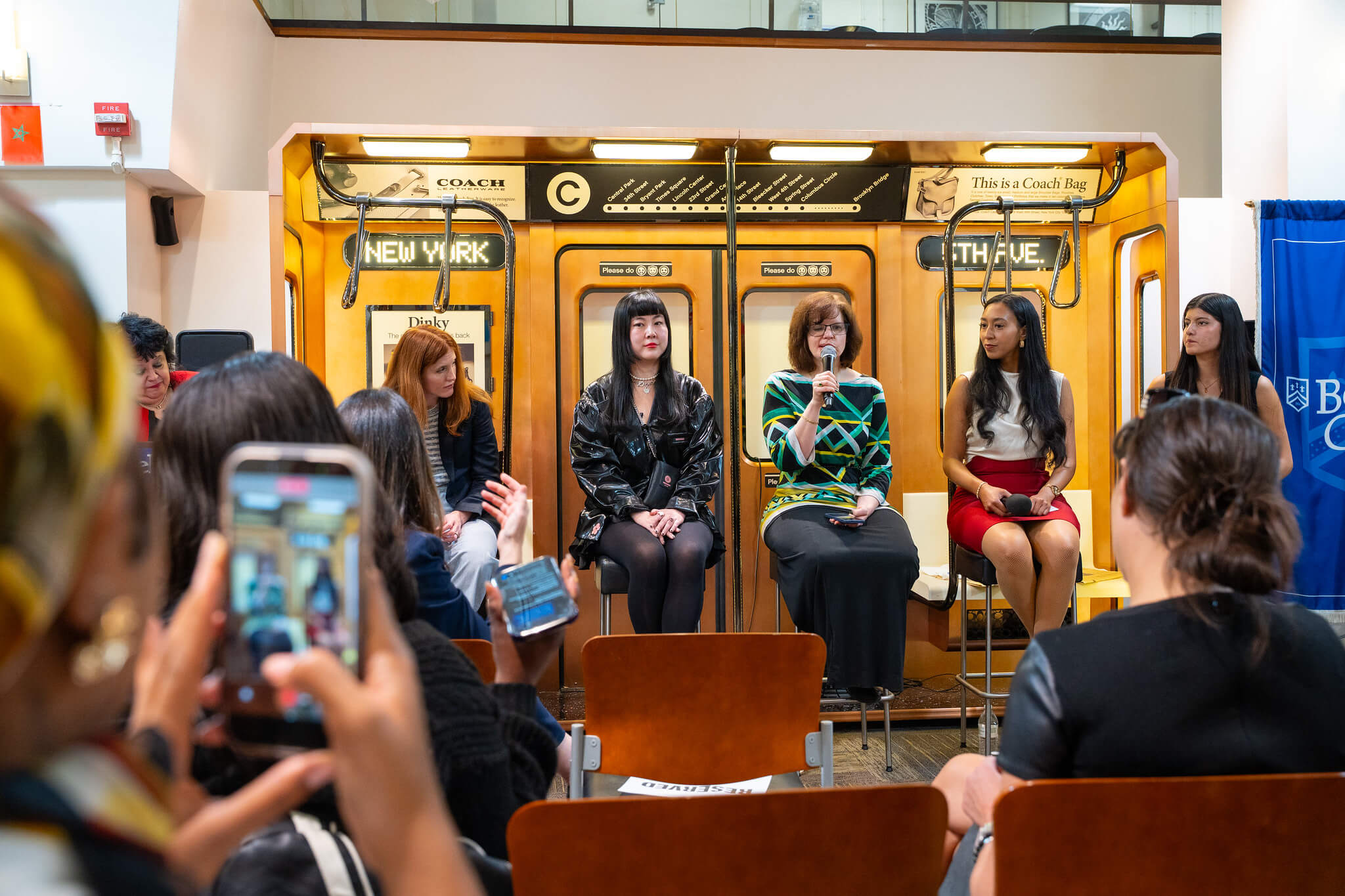 Panel discussion with four women seated inside a vintage New York subway car as an audience records the event.