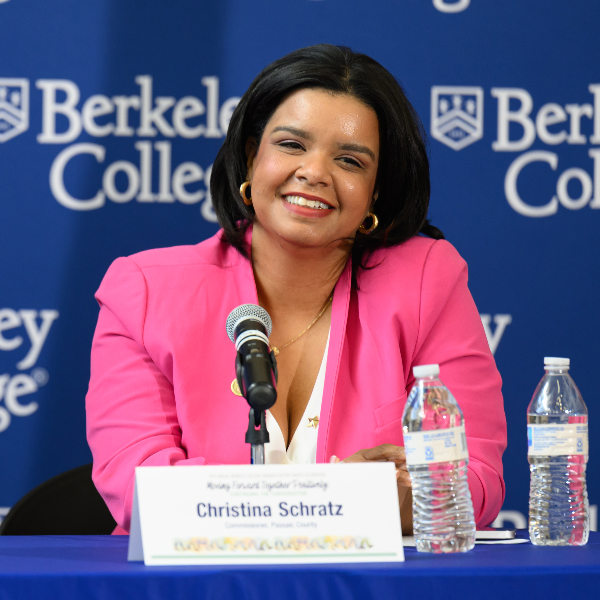 A woman in a pink suit jacket smiles