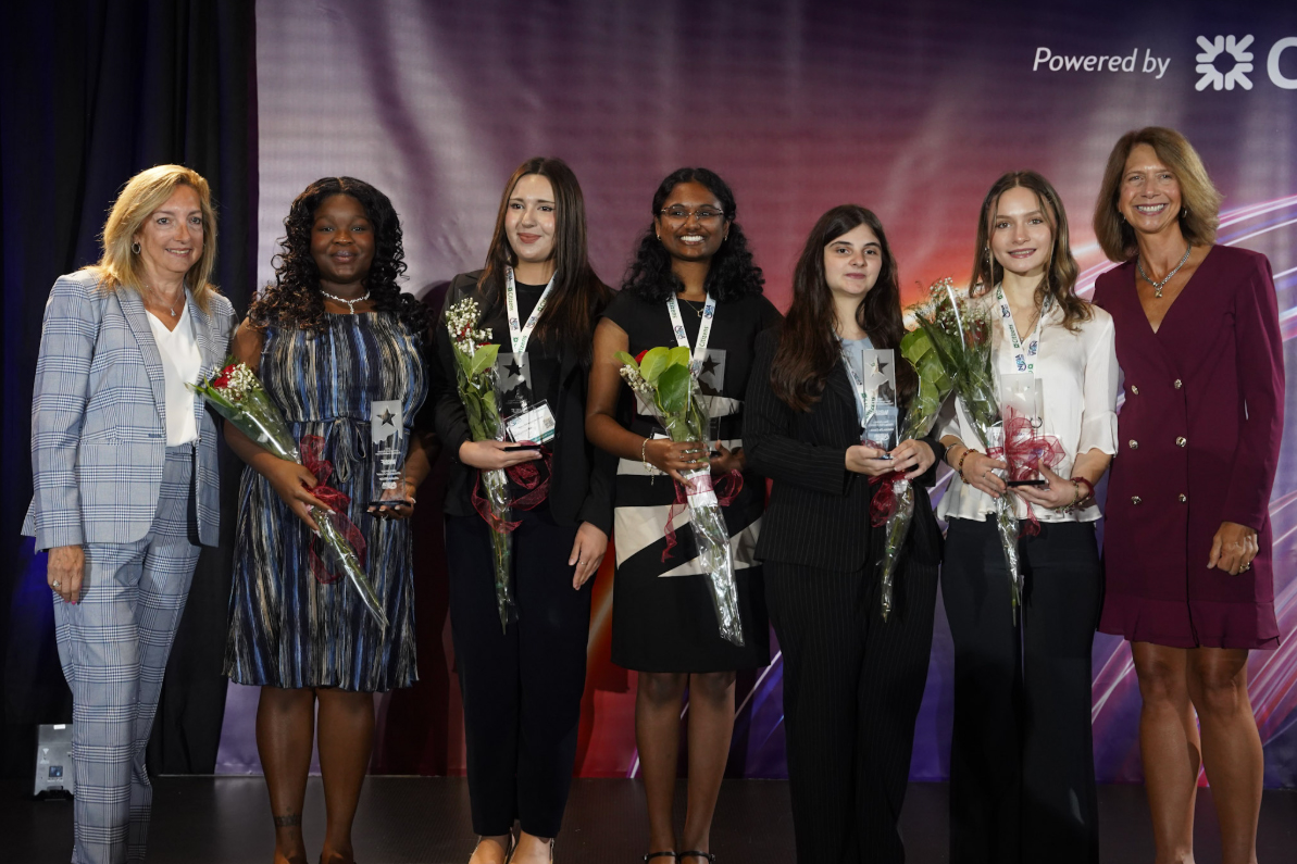 A group of young women stand on a stage holding awards and flowers