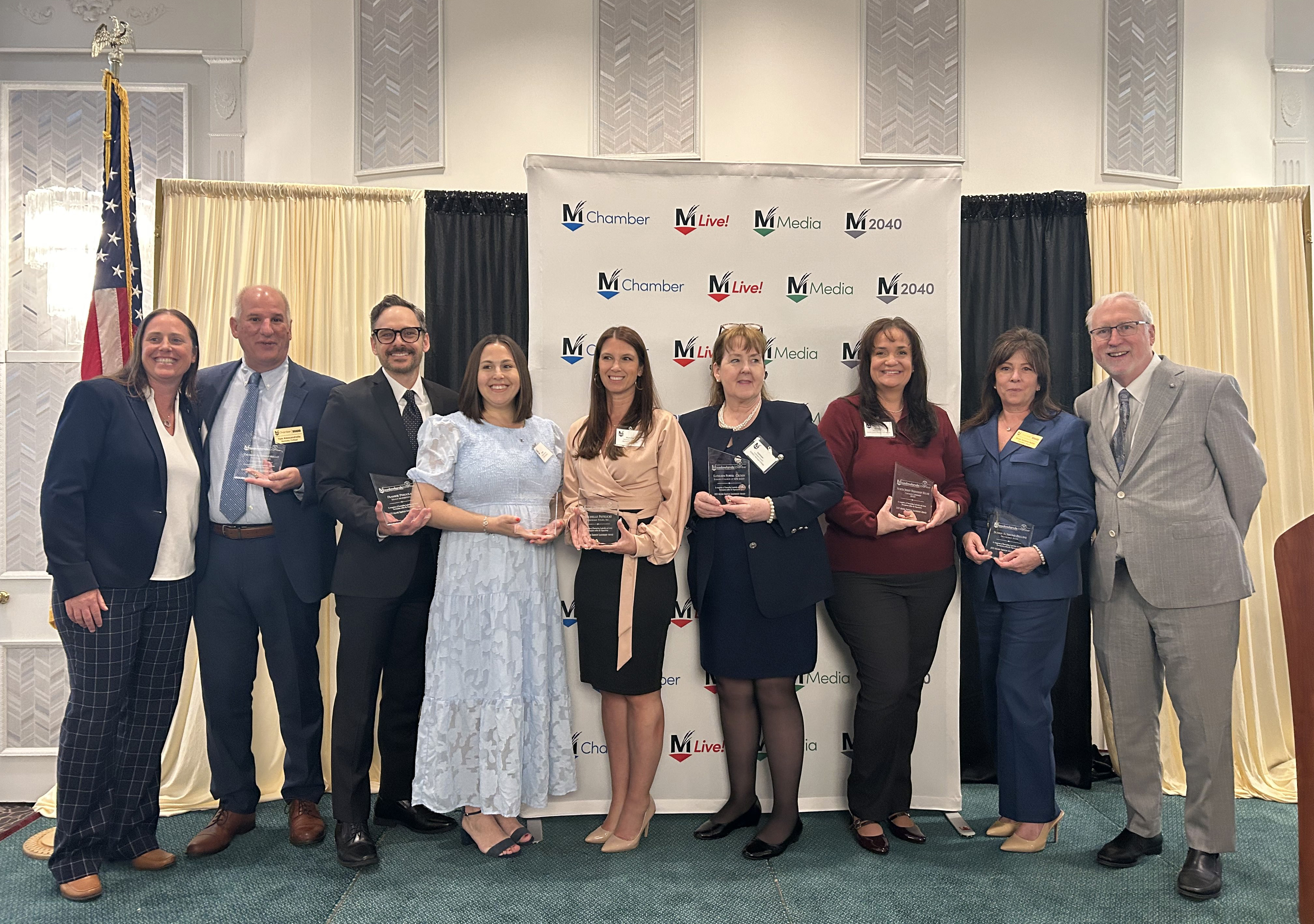 A group of individuals holds awards in front of a chamber of commerce backdrop.