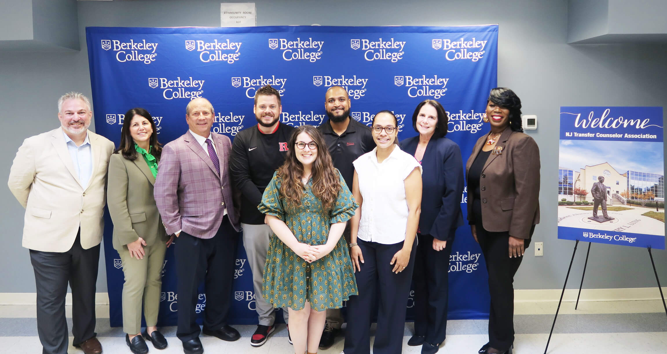 Eight people pose before a Berkeley College backdrop beside a welcome sign for the NJ Transfer Counselor Association.
