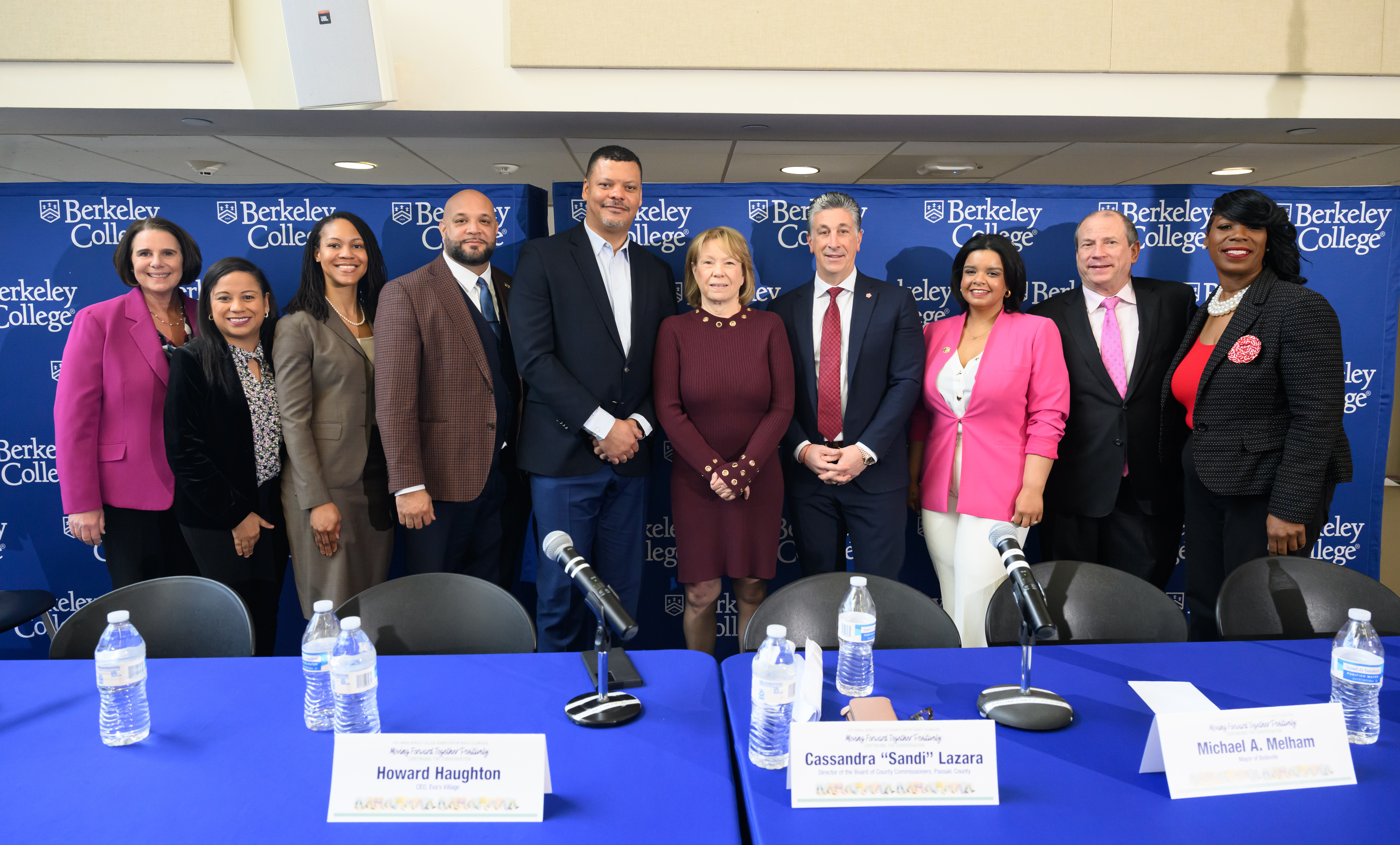 Community and college officials stand on a dais in front of a blue backdrop