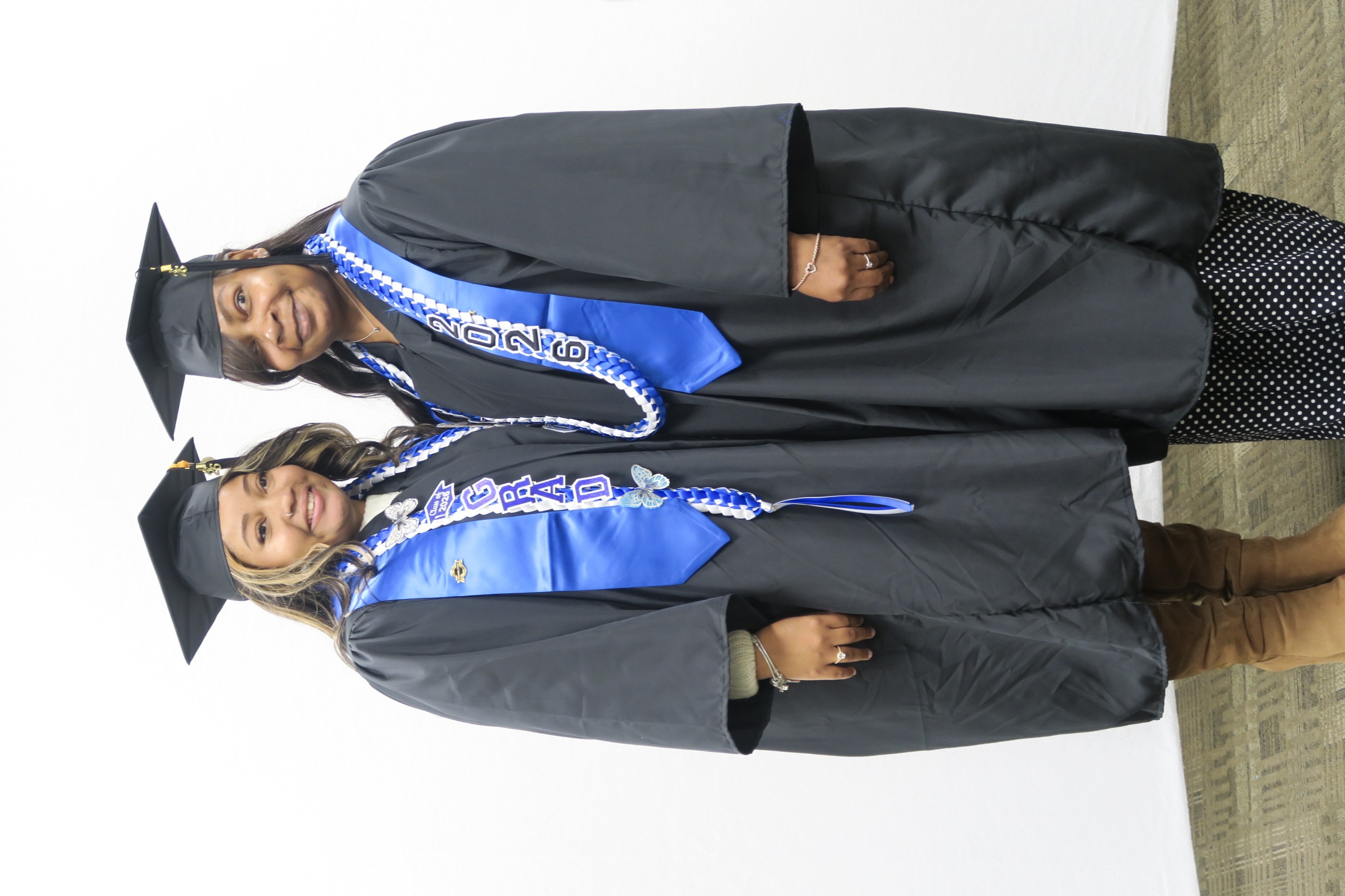 A mother and daughter stand smiling in graduation regalia.