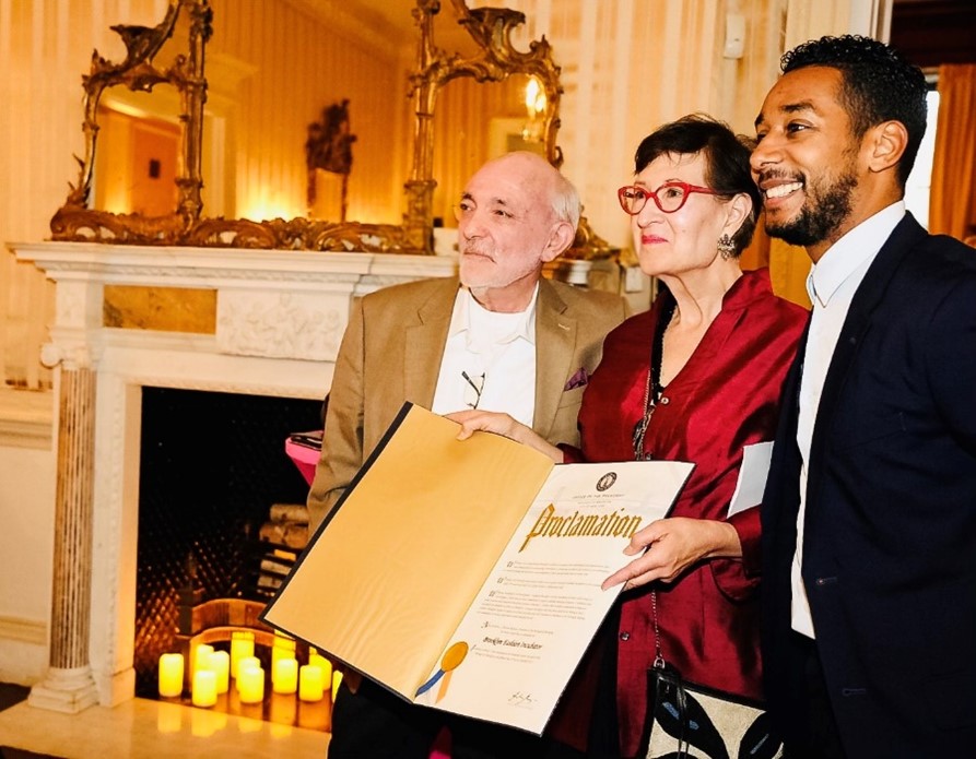 Two people receive a proclamation from a third person and all three smile and pose for the camera.
