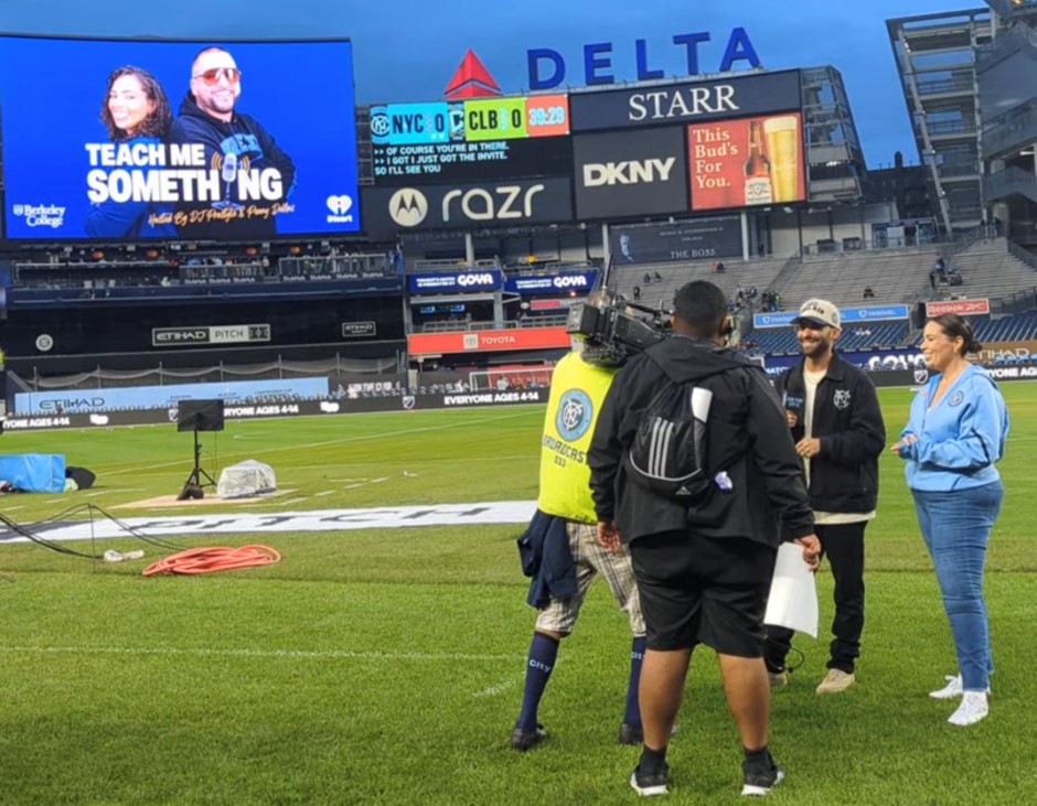 A woman and camera crew stand on a soccer field.
