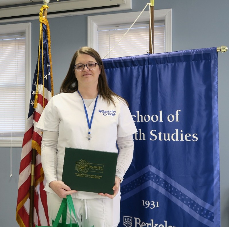 A woman in scrubs holds an award and smiles