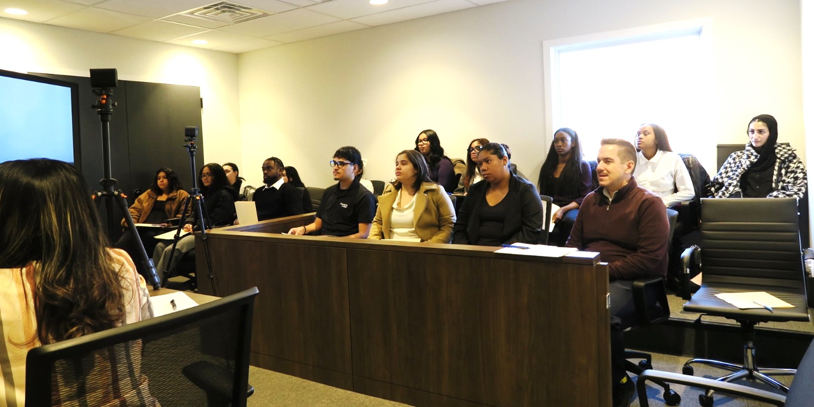 A group of students sits at a jury panel acting as jurors in a mock trial