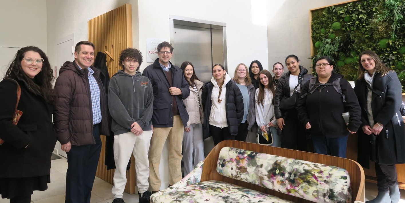 A group of diverse people stand smiling in a white lobby with a couch.